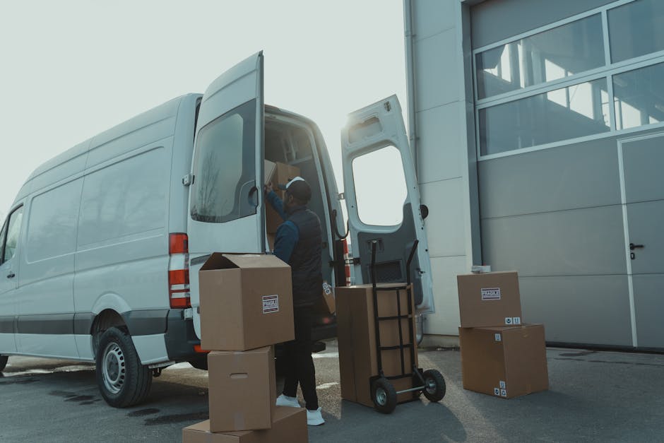 A professional mover from Islington Man and Van is standing outside a large grey commercial van with its rear doors open, loading packed cardboard boxes and household items into the vehicle during a h