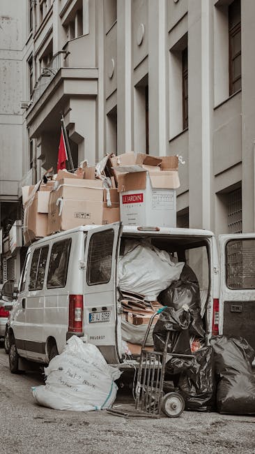 A professional mover from Islington Man and Van is standing outside a large grey commercial van with its rear doors open, loading packed cardboard boxes and household items into the vehicle during a h
